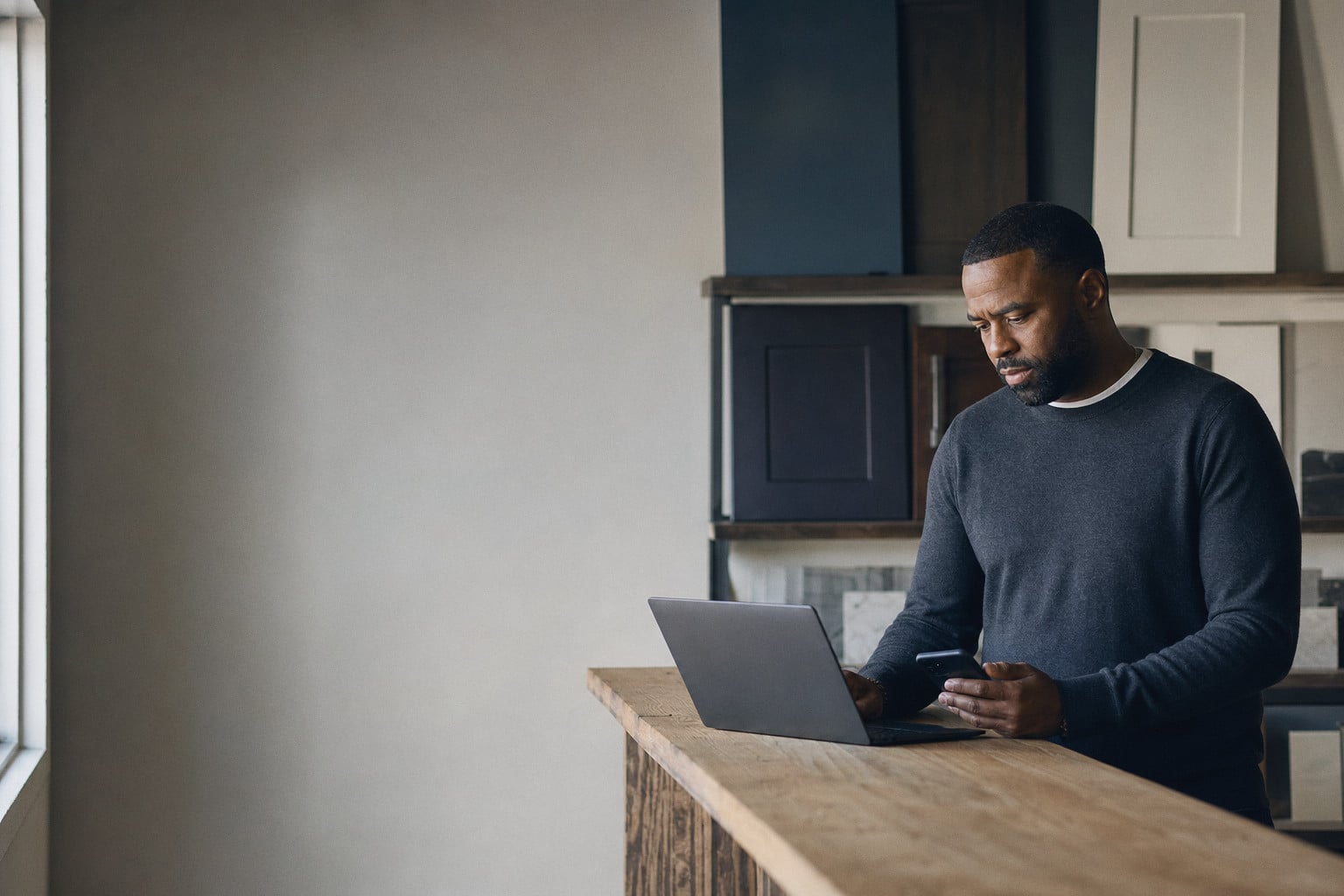A salesman in a showroom checks his phone beside an open laptop